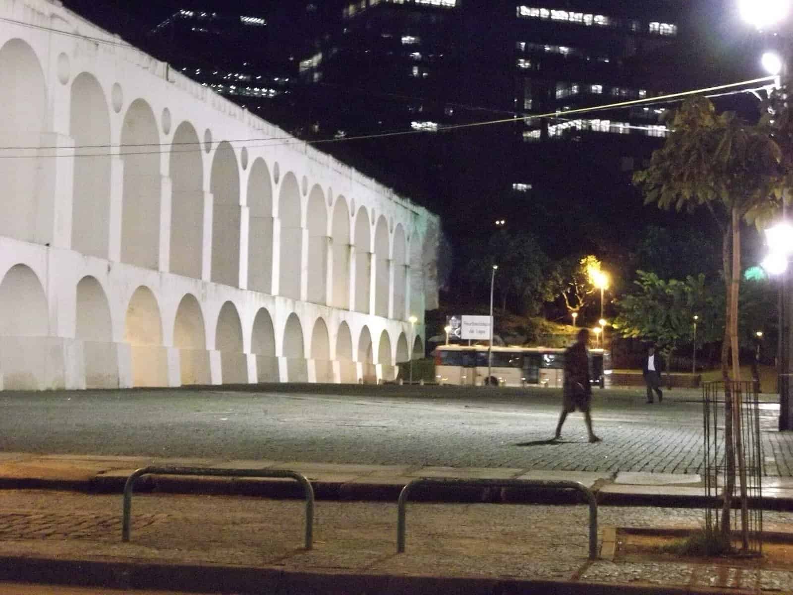 The white Arcos da Lapa aqueduct lit at night with office towers behind, central Rio de Janeiro