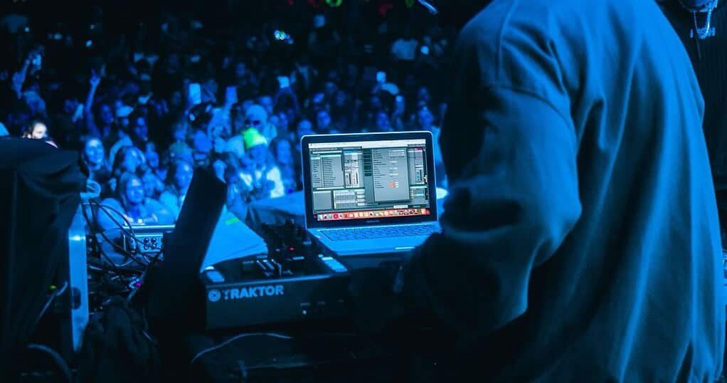 A techno DJ performing to a large festival crowd at night