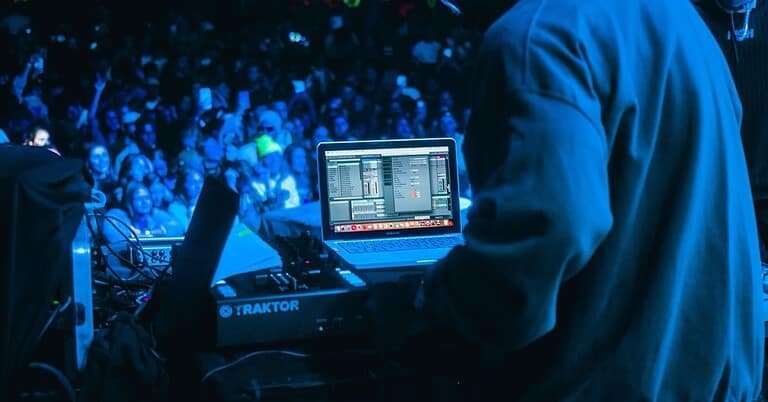 A techno DJ performing to a large festival crowd at night