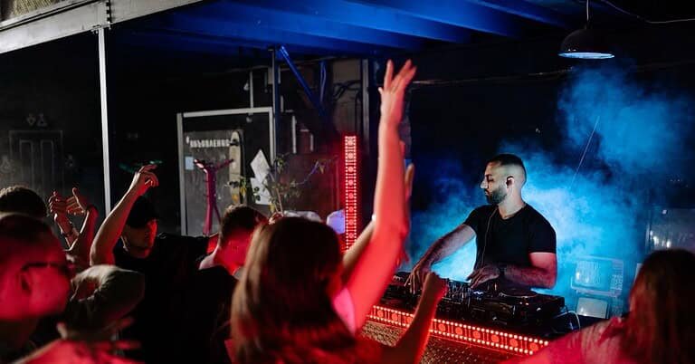 DJ playing to a crowd with raised hands in an underground club