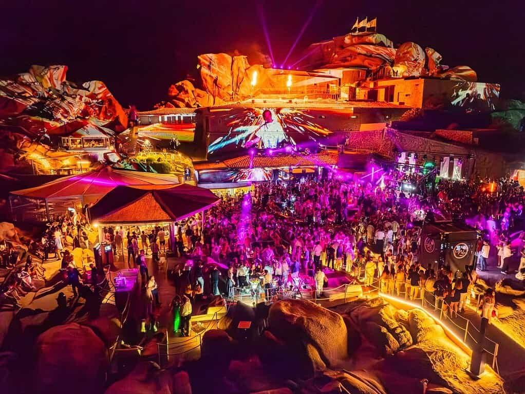 Crowd at Phi Beach Sardinia at night with projections mapped across the fortress rocks