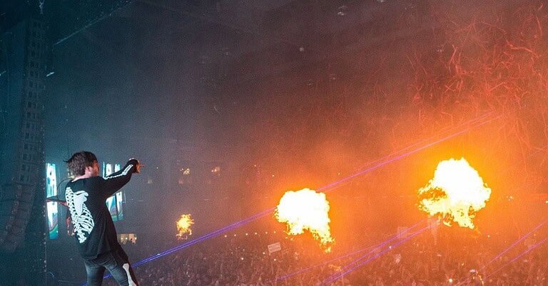Controlled flame jets fire from a festival Mainstage as a DJ performs, illustrating Tomorrowland 2026 weekend two pyrotechnics