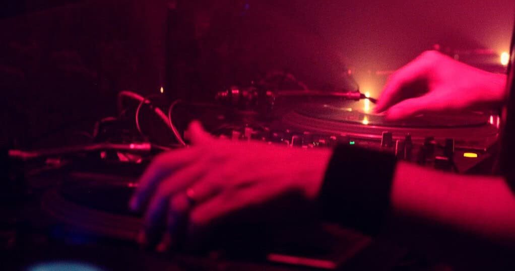 A DJ beatmatching two records in a club booth, the shared space behind every b2b set