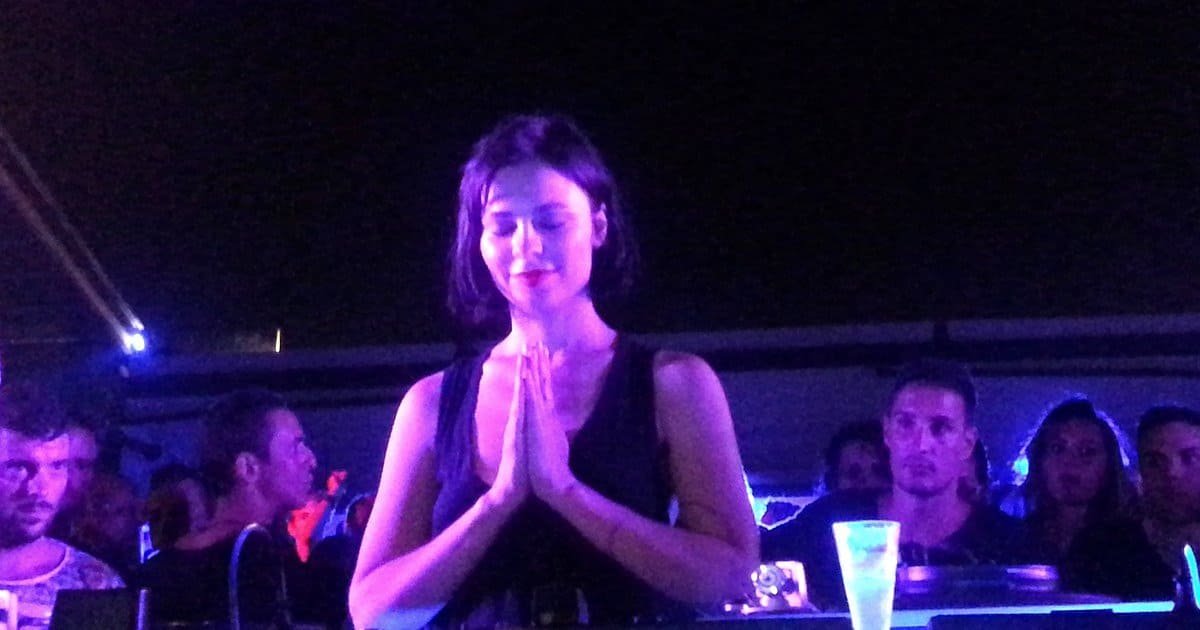 Nina Kraviz playing a DJ set behind the decks in a club booth Nina Kraviz playing a DJ set behind the decks in a club booth