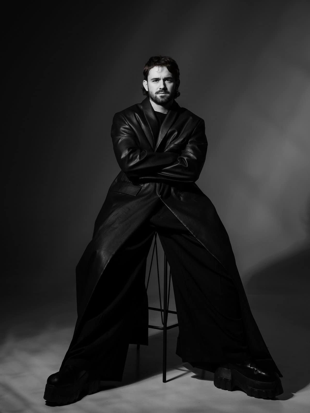 Black and white press portrait of Kevin Brauer seated on a stool