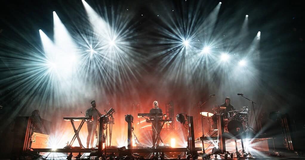 RÜFÜS DU SOL performing live on stage under white beams, the trio behind the highest-grossing electronic tour RÜFÜS DU SOL performing live on stage under white beams, the trio behind the highest-grossing electronic tour