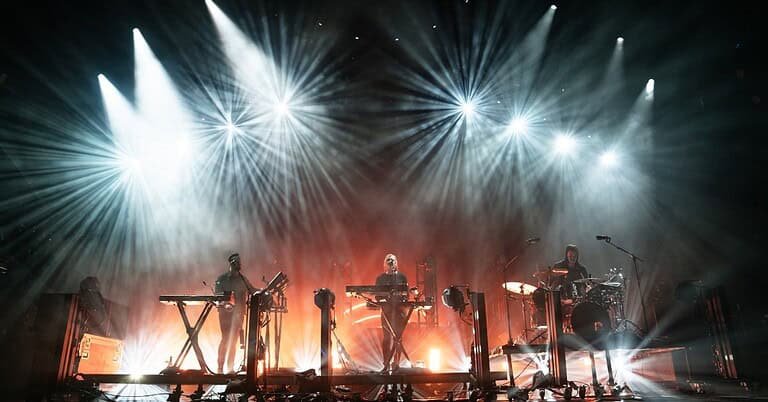 RÜFÜS DU SOL performing live on stage under white beams, the trio behind the highest-grossing electronic tour RÜFÜS DU SOL performing live on stage under white beams, the trio behind the highest-grossing electronic tour