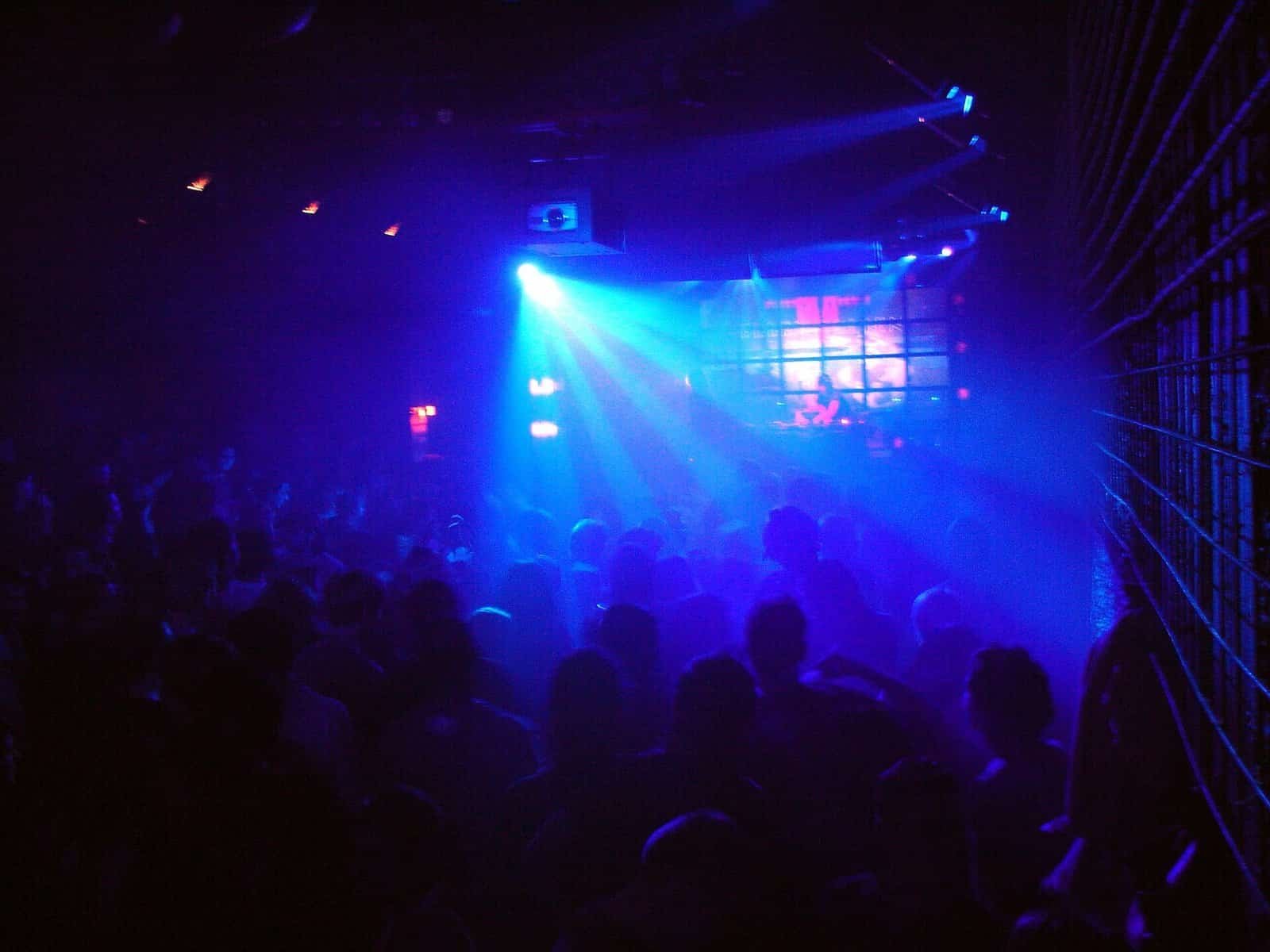 Techno Dance Moves: 7 Steps to Keep You Shining on the Dancefloor 1 Crowd dancing in a dark techno club under blue stage lights, with the DJ booth and video wall at the back