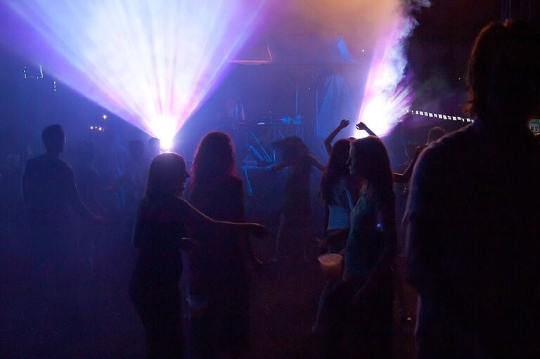 People dancing at a night techno party under purple and white stage lights People dancing at a night techno party under purple and white stage lights