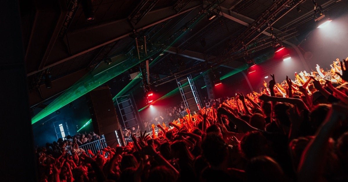 Crowd with raised hands under green lasers at an Amsterdam Dance Event club night