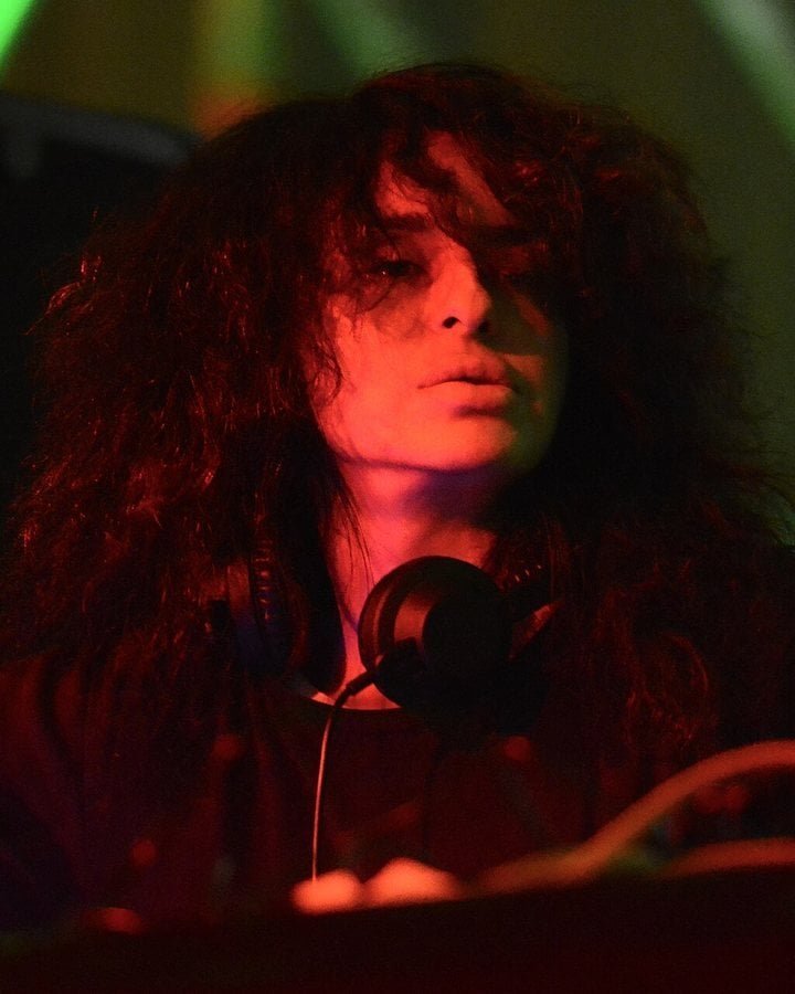 Highest-Paid Female Techno DJs 2026: Amelie Lens, Charlotte de Witte and 12 More 9 Nicole Moudaber with headphones round her neck under red stage light at Mayday 2014