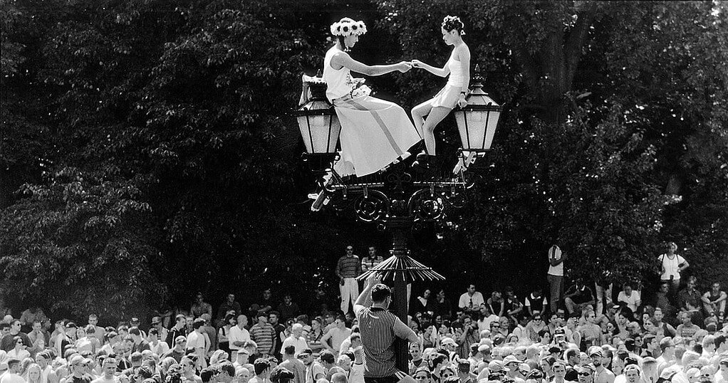 Two ravers in flower crowns on a lamp post above the crowd at Love Parade Berlin 1996, the era of classic rave culture movies