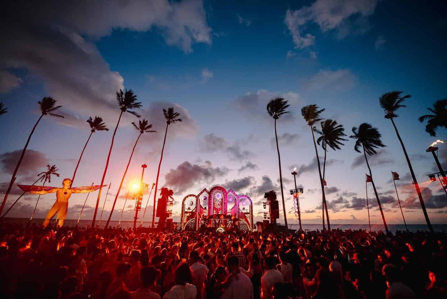 Crowd under palm trees at the Réveillon Carneiros beach stage at sunset in Pernambuco, Brazil Crowd under palm trees at the Réveillon Carneiros beach stage at sunset in Pernambuco, Brazil
