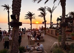 Sunset over the sea at Scorpios in Paraga, Mykonos, seen through the palm trees above the beach club Sunset over the sea at Scorpios in Paraga, Mykonos, seen through the palm trees above the beach club