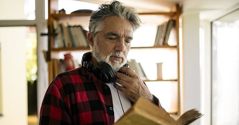Man reading a book with headphones around his neck, illustrating the link between techno music and intelligence
