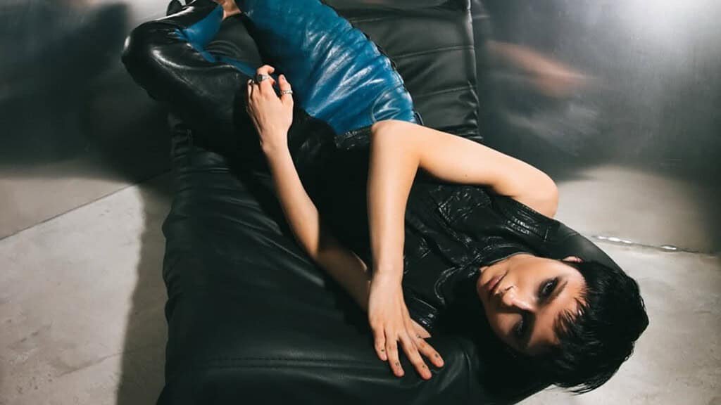The Aksis, Anna Kuprienko, lying on a black leather sofa, Quit It artwork